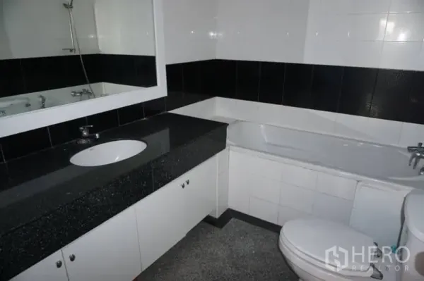 Condominium for rent in Watthana, Bangkok - Black and white tiled bathroom featuring a bathtub, large mirror and under‑counter storage.