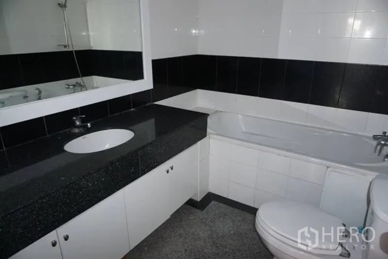 Condominium for rent in Watthana, Bangkok - Black and white tiled bathroom featuring a bathtub, large mirror and under‑counter storage.