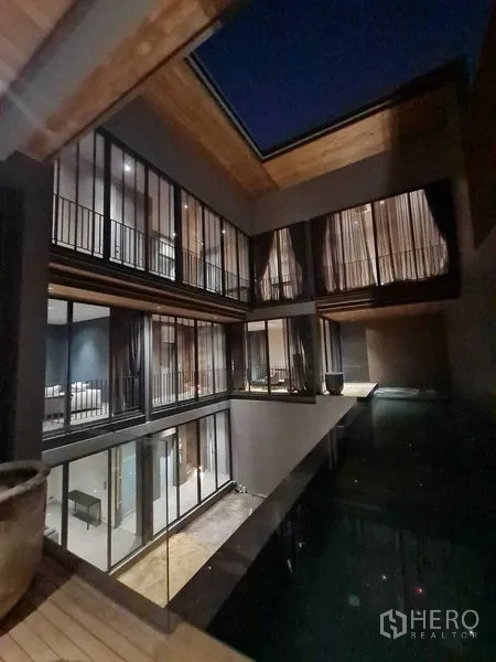 独立式住宅 出售在Lat Phrao, Bangkok - 夜色中的庭院，中庭泳池环绕玻璃卧室。