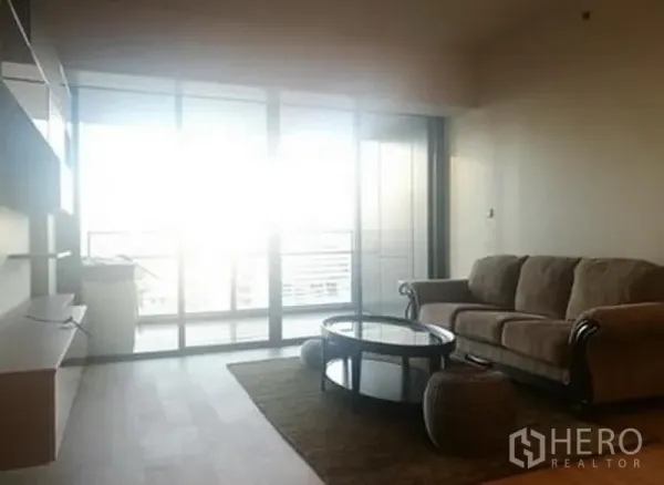 Condominium for sale in Sathon, Bangkok - Bright living room in a Sathon condo with sofa, round coffee table and floor‑to‑ceiling glass doors to a balcony city view.