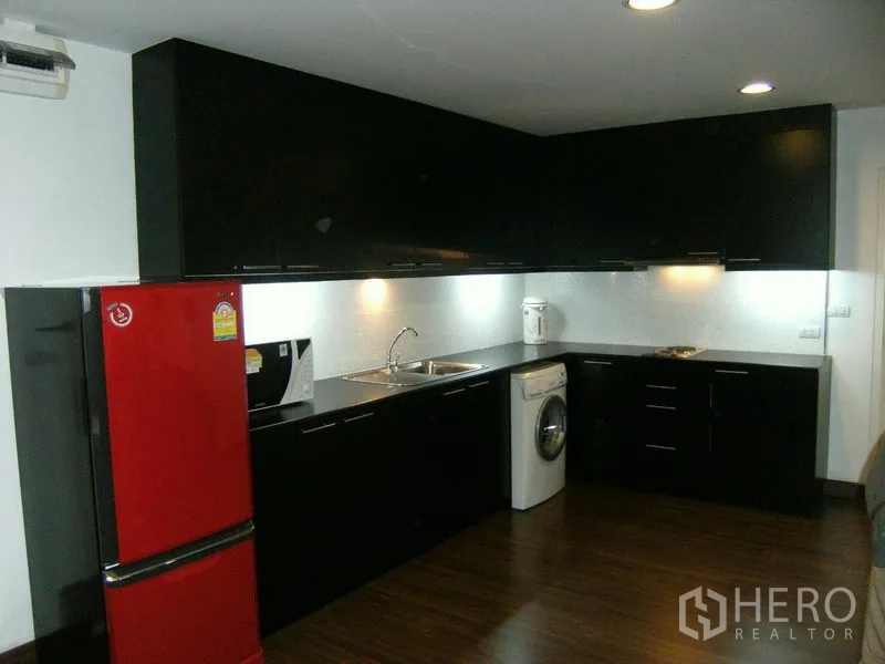 Condominium for rent in Watthana, Bangkok - Full fitted kitchen with black cabinetry, red refrigerator, sink, and under-cabinet lighting.
