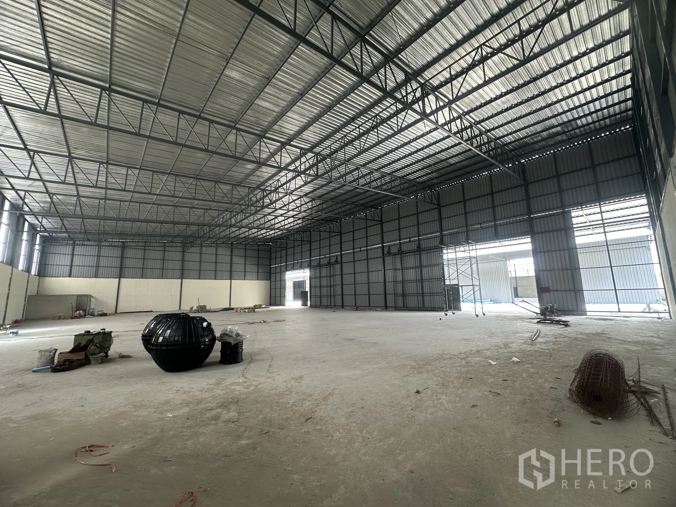 Warehouse for rent in Lam Luk Ka, Pathum Thani - Spacious warehouse interior with steel truss roof, smooth concrete floor, and large door opening.