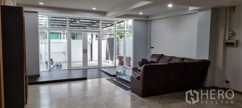 Townhouse for rent in Watthana, Bangkok - Open-plan living area with recessed lighting and a raised platform beside floor-to-ceiling windows.