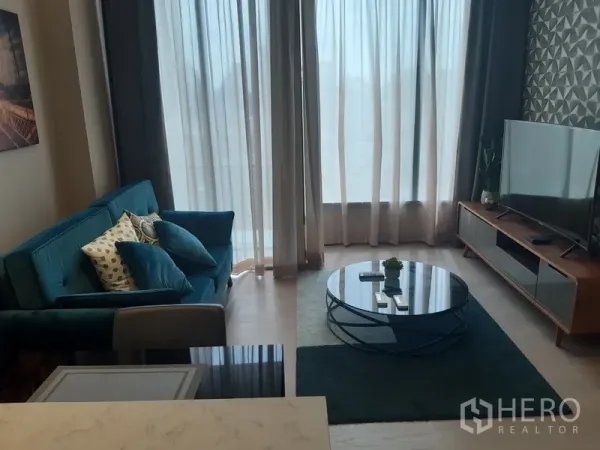 Condominium for rent or sale in Watthana, Bangkok - Bright living room with sheer curtains, teal sofa, round glass coffee table and media console.