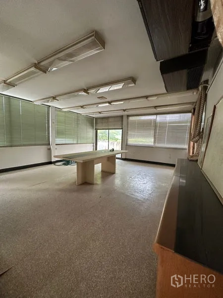 Shophouse for rent in Sathon, Bangkok - Bright corner room with wraparound windows, blinds, and a central table.