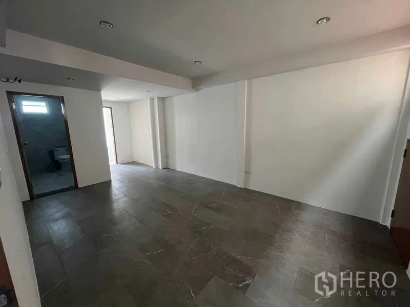 Townhouse for rent in Khlong Toei, Bangkok - Large multipurpose room with dark floor tiles and access to a bathroom.
