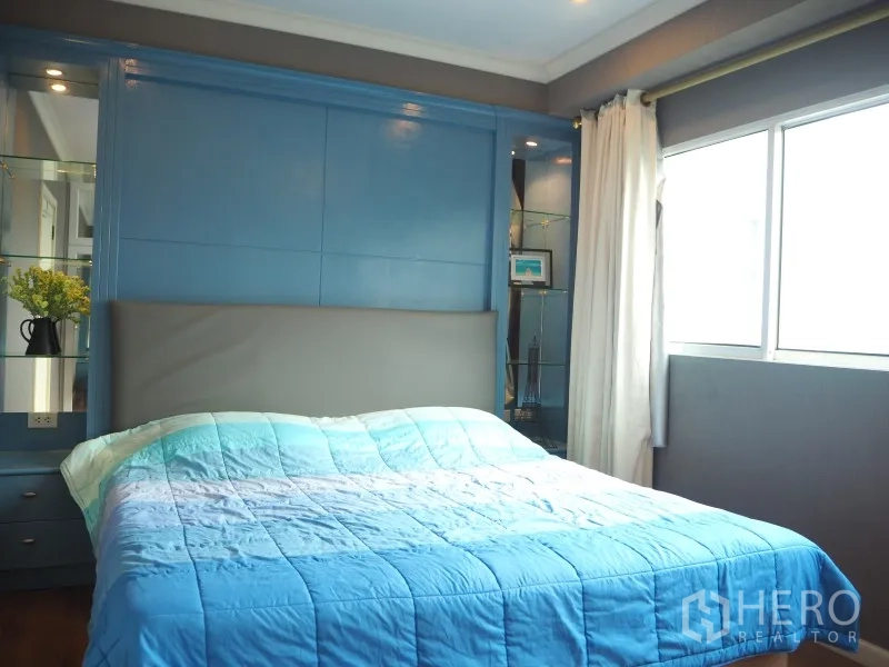 Condominium for rent or sale in Watthana, Bangkok - Master bedroom with blue feature wall, double bed, glass display shelves, and natural light.
