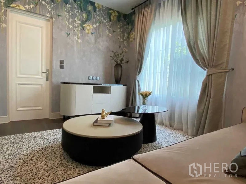 独立式住宅 出租在Bang Khen, Bangkok - 次起居室，花卉主题墙、纱帘与圆形茶几。