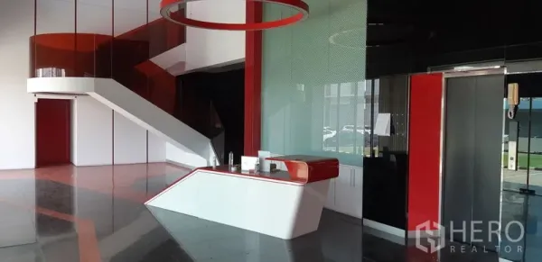 Factory for rent in Lat Krabang, Bangkok - Modern reception lobby with red-and-white desk and a curved staircase inside the factory office.