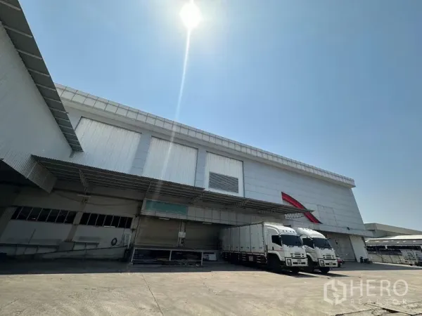 货栈 出租在Lam Luk Ka, Pathum Thani - 仓库正面宽阔，多个装卸月台，两辆卡车停靠作业。