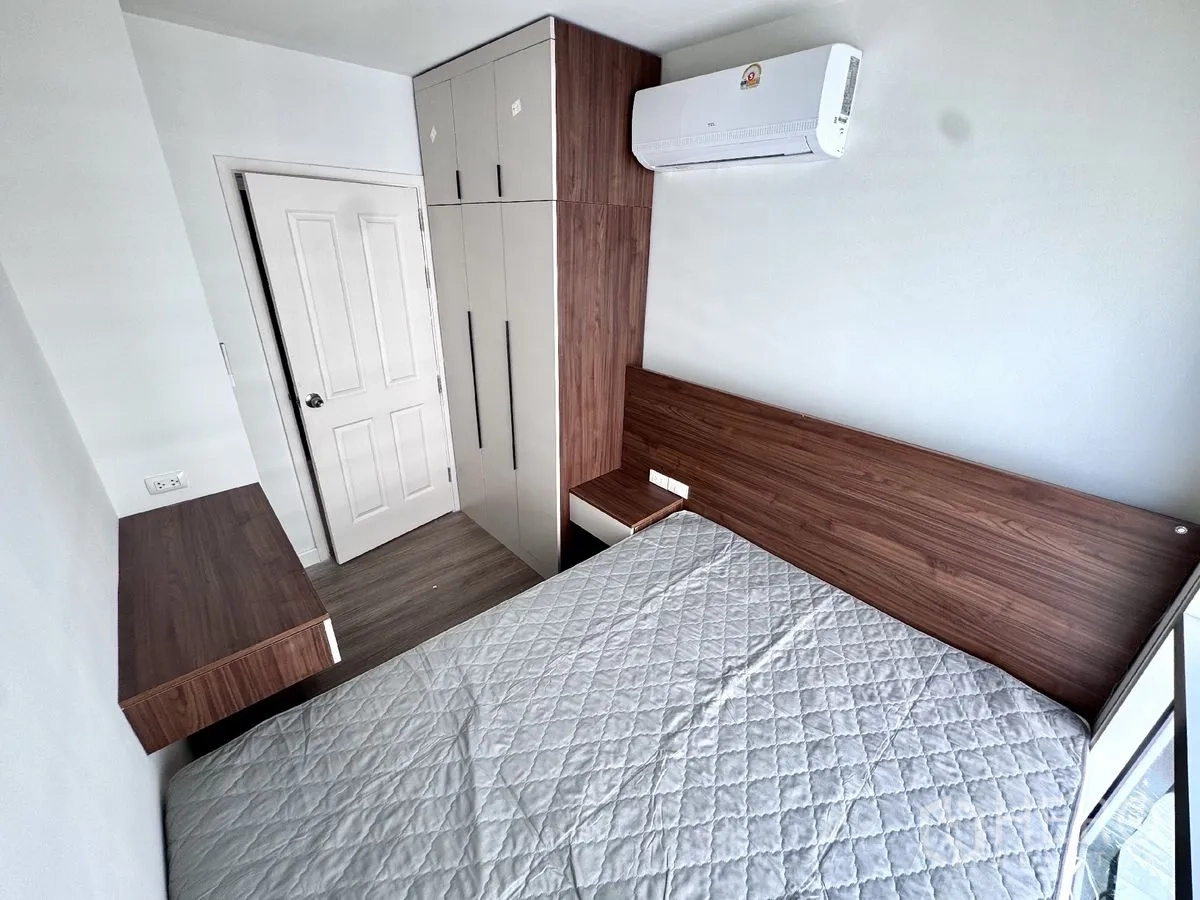 Condominium for rent in Huai Khwang, Bangkok - Compact bedroom with bed, built-in wardrobe, desk, and wall-mounted air conditioner.