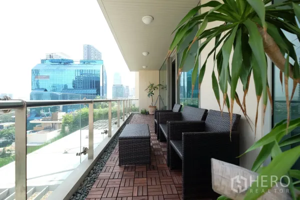 公寓 出租在Bang Rak, Bangkok - The Legend Saladaeng 宽景阳台，藤椅、木地板与玻璃栏杆，俯瞰是隆天际线。