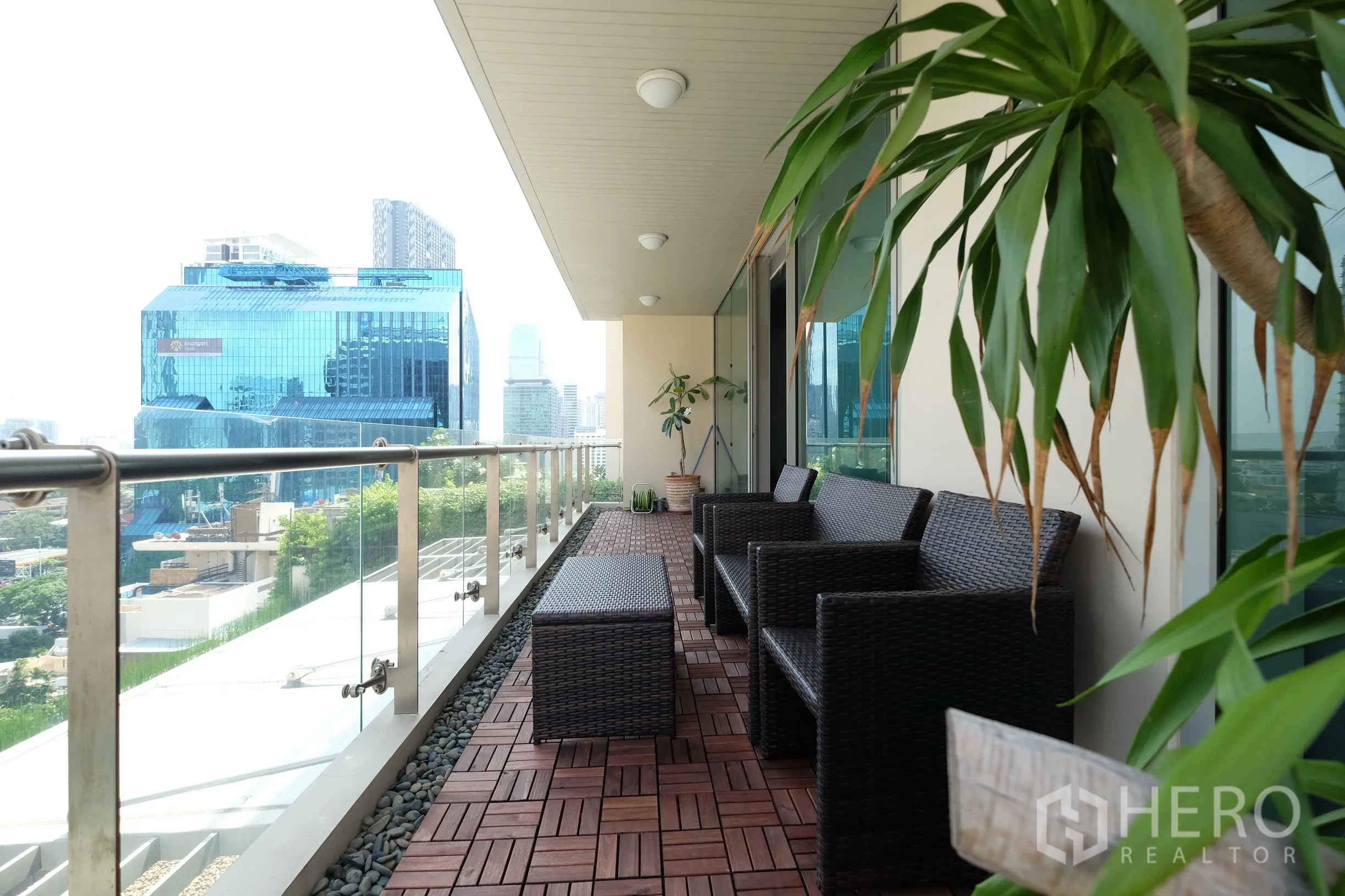 公寓 出租在Bang Rak, Bangkok - The Legend Saladaeng 宽景阳台，藤椅、木地板与玻璃栏杆，俯瞰是隆天际线。