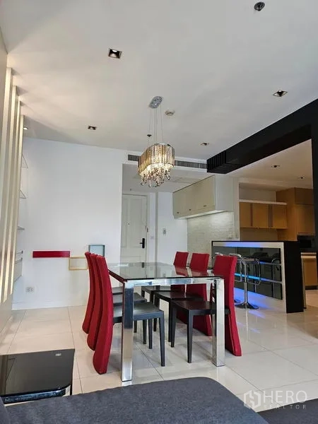 Condominium for rent or sale in Pathum Wan, Bangkok - Dining area with glass table, red chairs and crystal chandelier beside an open kitchen.