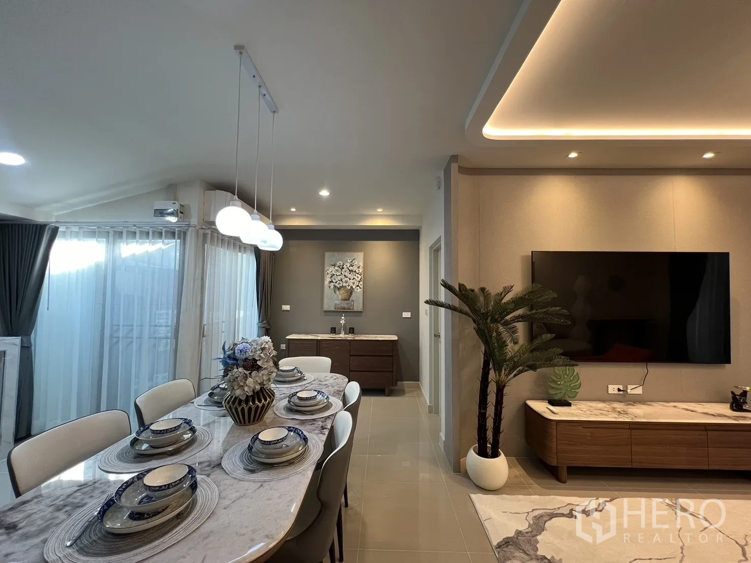 Townhouse for rent in Bang Phli, Samut Prakan - Dining table beside a TV console and potted plant under warm ambient lighting.