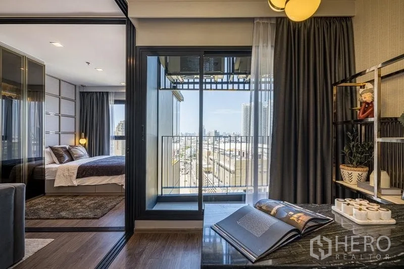 Condominium for sale in Chatuchak, Bangkok - Compact balcony and study nook with sliding glass doors connecting to the bedroom and city skyline beyond.