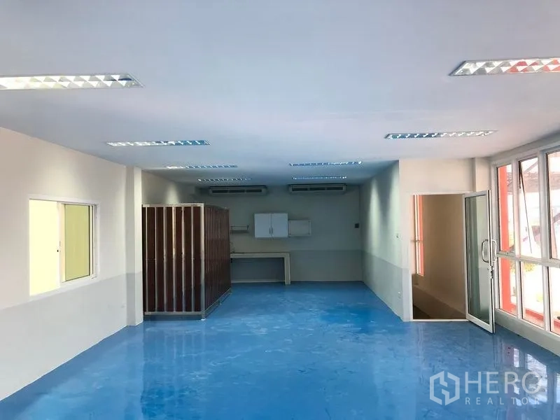 Factory for rent in Samut Prakan - Bright office workspace with blue epoxy flooring, air conditioners and a glass entry door.