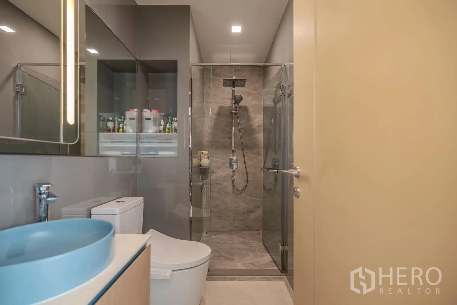 Condominium for rent in Watthana, Bangkok - Modern bathroom with glass-enclosed shower, blue vessel sink and toilet.