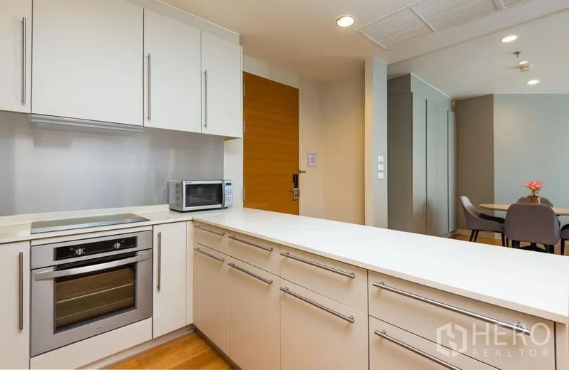 Condominium for rent in Bang Kho Laem, Bangkok - Modern L-shaped kitchen with oven, microwave and white cabinetry.
