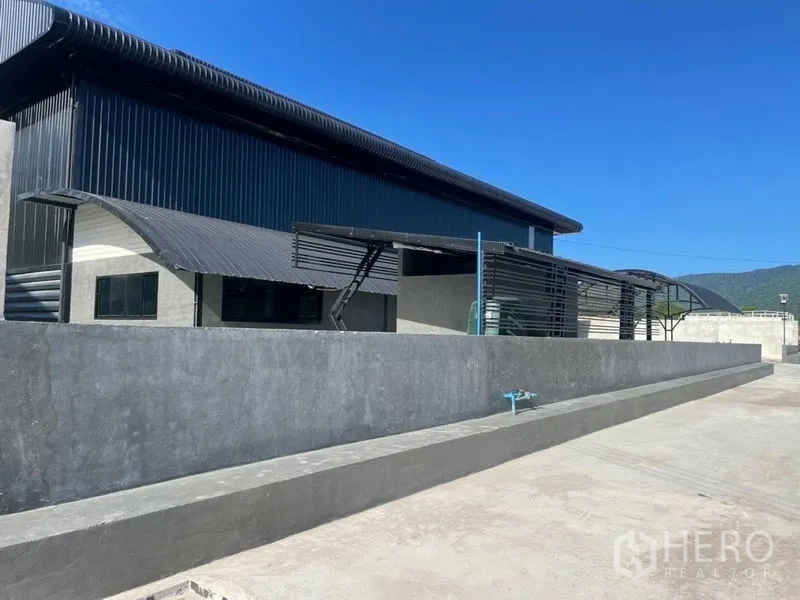Warehouse for rent in Ban Bueng, Chon Buri - Side elevation of a steel-clad warehouse with a long loading platform and mountain backdrop.