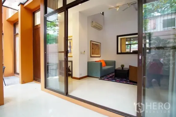 Townhouse for rent in Watthana, Bangkok - Sliding glass doors opening to a bright living area with sofa and wall mirror.