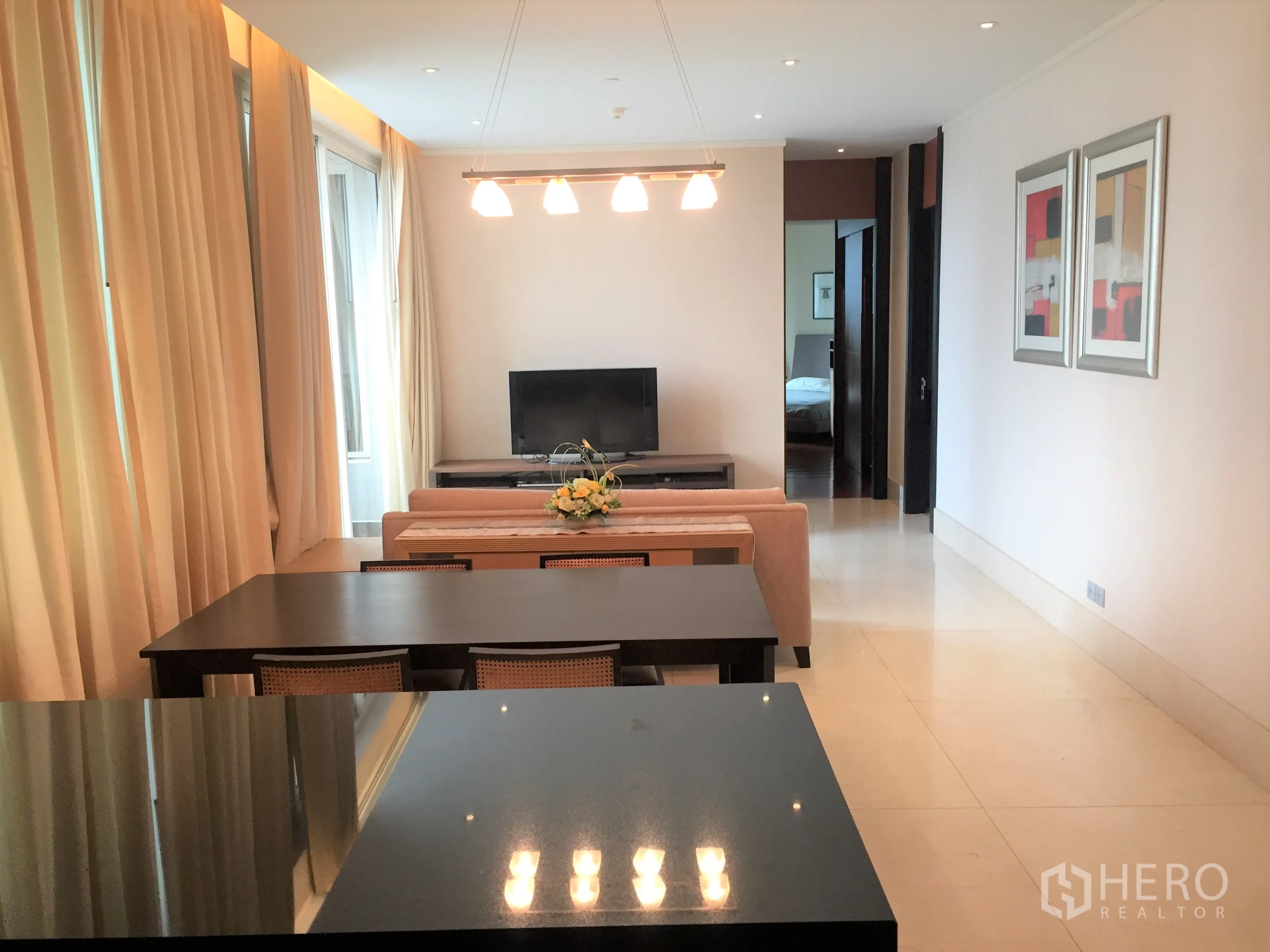 Condominium for rent in Bang Rak, Bangkok - Open-plan dining and living area with long table, sofa and TV in a bright neutral palette.