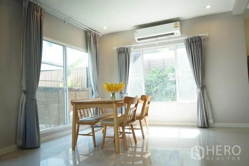Detached House for rent in Bang Phli, Samut Prakan - Bright dining area with wooden table, large windows, curtains and wall-mounted air conditioner.