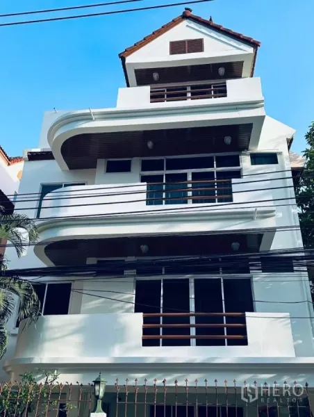 บ้าน ให้เช่า - บ้านเดี่ยวหลายชั้นในเขตวัฒนา กรุงเทพฯ ตัวอาคารสีขาวระเบียงโค้งและหลังคากระเบื้อง.