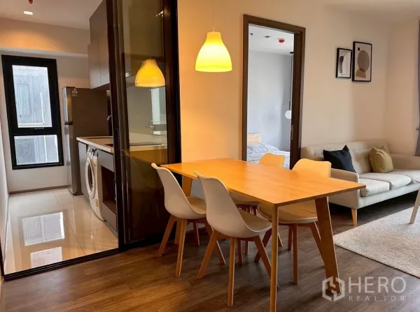 Condominium for rent in Chatuchak, Bangkok - Dining area next to enclosed kitchen with pendant light and sofa view.