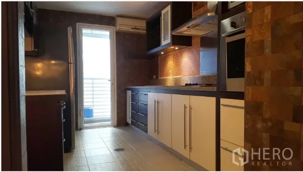 Condominium for rent in Watthana, Bangkok - Galley kitchen with built-in oven and cooktop, mosaic backsplash, ample cabinets, and a door to the service balcony.