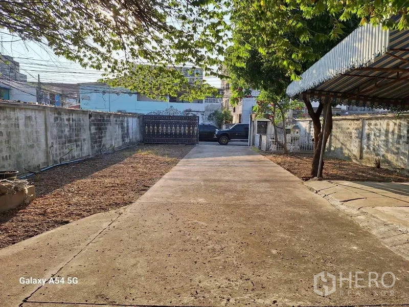 独立式住宅 出租在Bang Na, Bangkok - 宽阔混凝土车道，带遮雨车棚与充足停车空间。