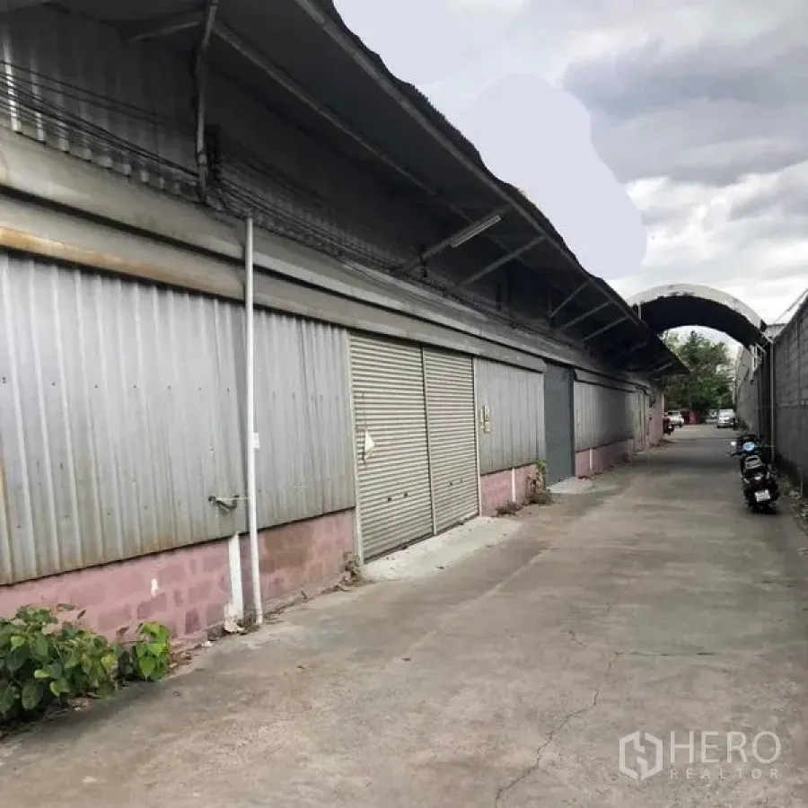 货栈 出租在Khan Na Yao, Bangkok - 金属板外墙的仓库外观，卷帘门沿约5米宽通道分布。