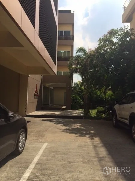 Home Office for sale in Phra Khanong, Bangkok - Private driveway and parking area between buildings with mature greenery.