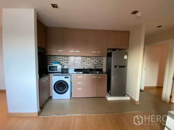 公寓 出租在Khlong Toei, Bangkok - 开放式厨房，木色橱柜与马赛克墙砖，配灶台、微波炉、冰箱和洗衣机。