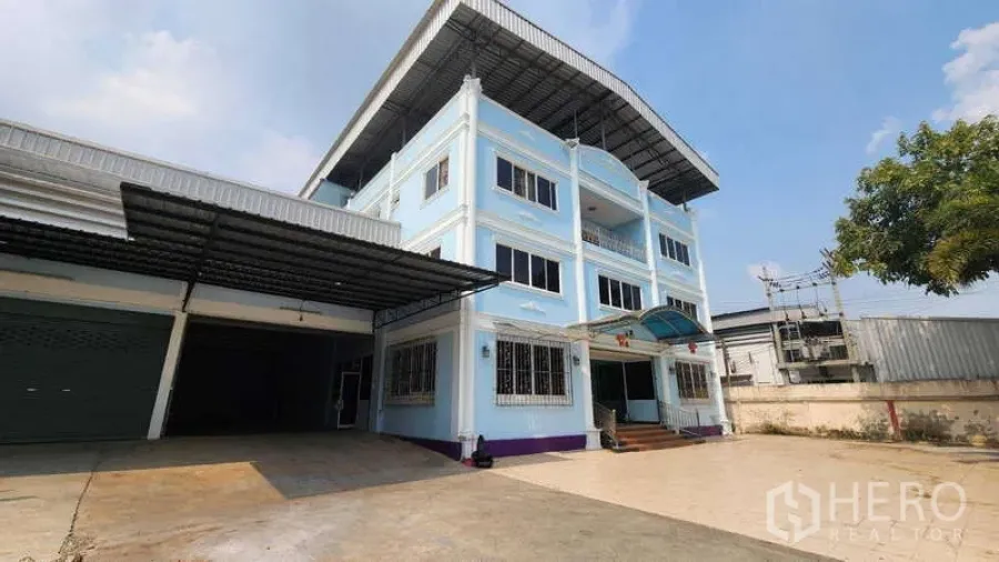 Factory for rent in Pak Kret, Nonthaburi - Three-storey blue office building attached to a warehouse with wide driveway and covered loading bay