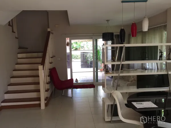 Townhouse for rent or sale in Bueng Kum, Bangkok - View of staircase and living area with tiled floors and wide sliding doors opening to a terrace with garden views.