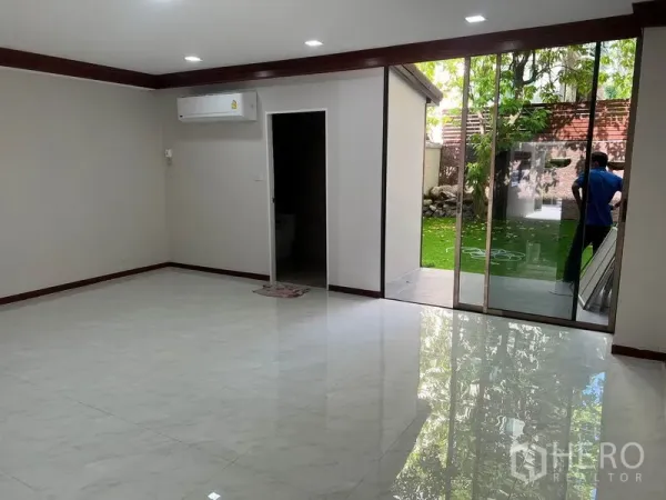 Townhouse for rent in Watthana, Bangkok - Bright living room with recessed lights and full-height sliding doors opening to a private lawn.