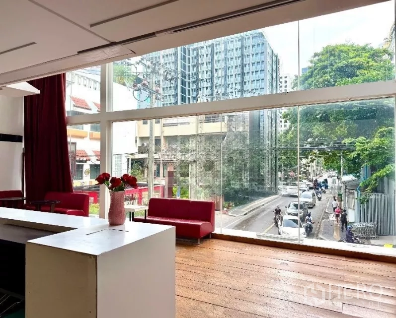 零售空间 出租在Watthana, Bangkok - 明亮的零售楼层，落地窗、红色沙发与木地板，面向城市街景。