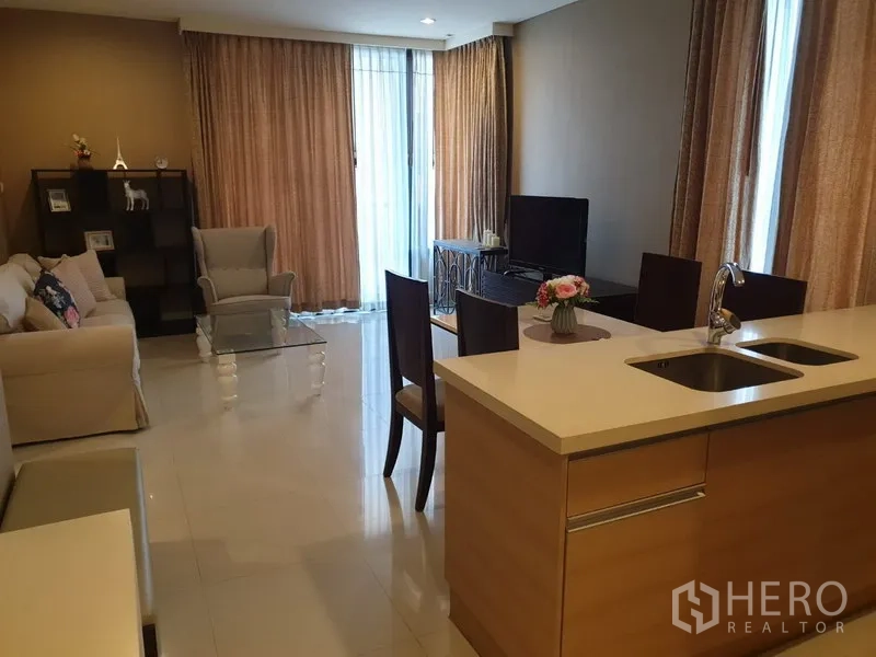 Condominium for rent in Khlong Toei, Bangkok - Bright living and dining area with glass coffee table, sofa set, TV console, and floor-to-ceiling windows with curtains.