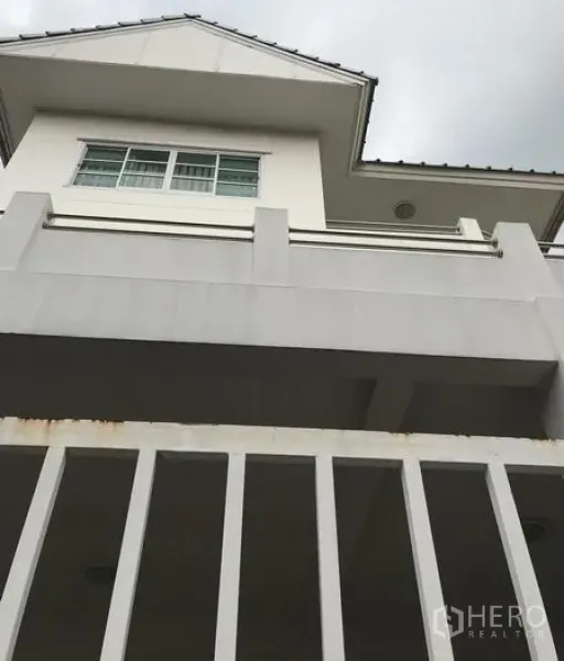 Detached House for rent in Din Daeng, Bangkok - Low-angle view of a modern detached house exterior with balcony, white facade and windows behind a gated fence.