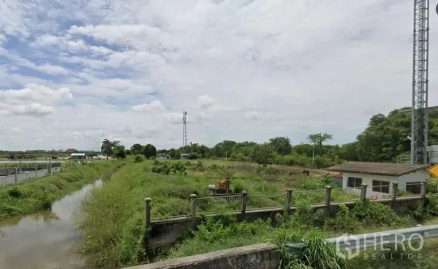 Land for sale in Bang Sao Thong, Samut Prakan - Canal running along the land boundary with green vegetation, tower and small building in view.