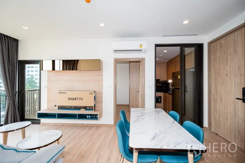 คอนโด ให้เช่าในWatthana, Bangkok - ผนังทีวีและพื้นที่ทานอาหารหันสู่ระเบียง มีประตูบานเลื่อนไปยังครัวปิด