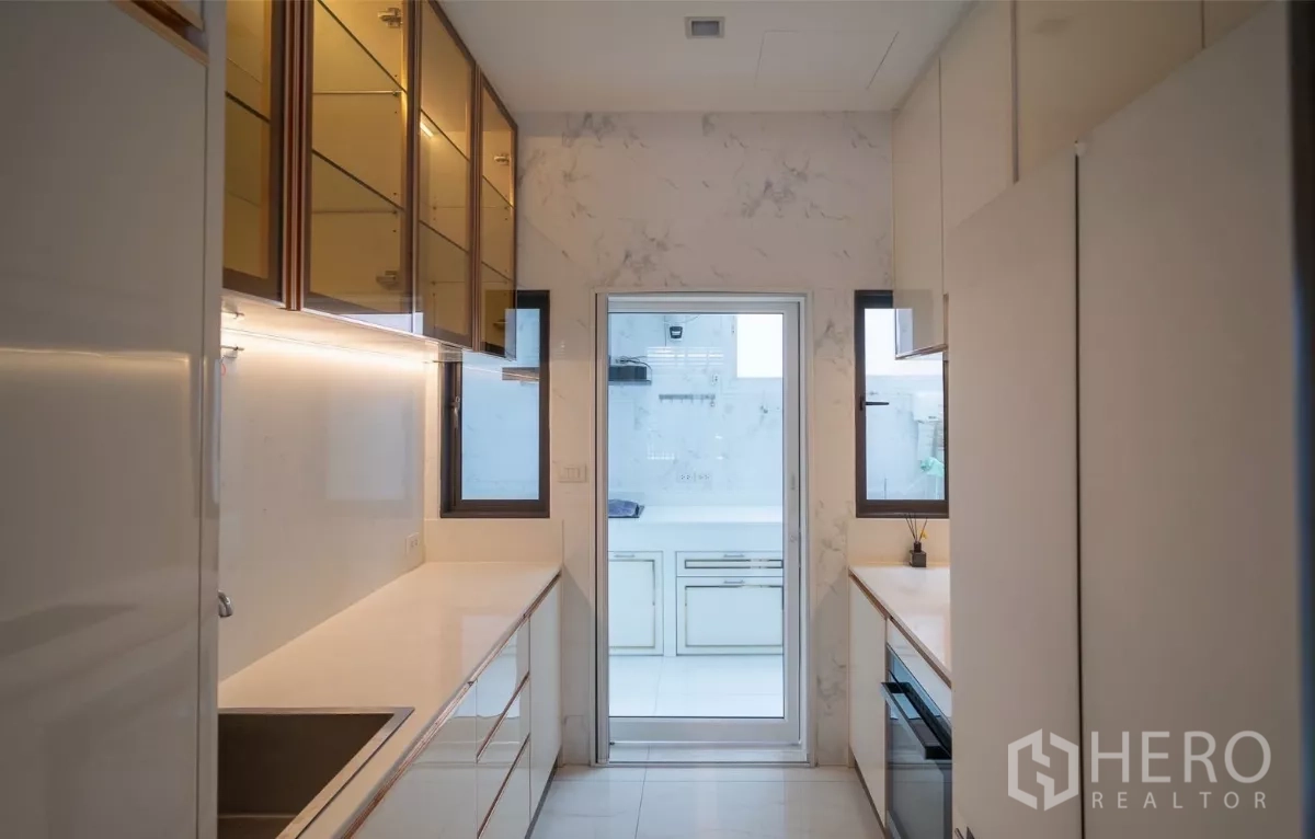 Detached House for rent or sale in Saphan Sung, Bangkok - Sleek galley kitchen with glossy cabinetry and door leading to the Thai kitchen.