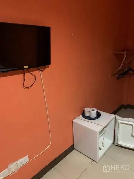พื้นที่ขายปลีก ให้เช่าในKhlong Toei, Bangkok - ทีวีติดผนังและตู้เย็นเล็กเปิดอยู่ พร้อมชั้นแขวนในห้องพัก