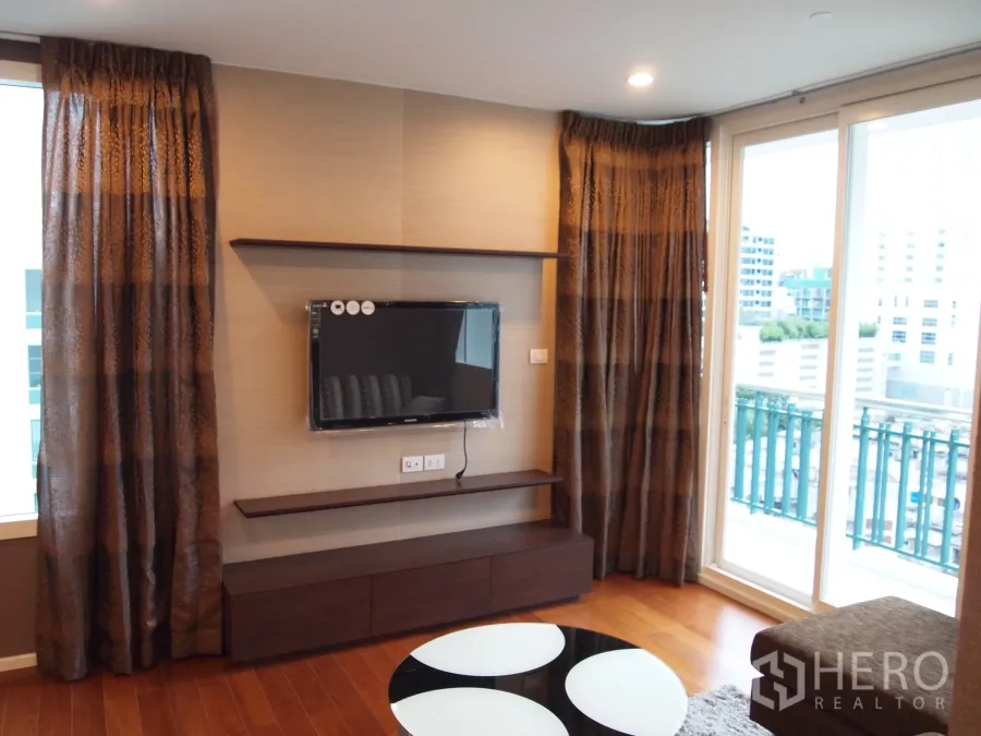 คอนโด ให้เช่าหรือขายในWatthana, Bangkok - ห้องนั่งเล่นมีทีวีติดผนัง ประตูกระจกบานเลื่อนออกสู่ระเบียงชมวิวเมือง ที่ Wind Sukhumvit 23