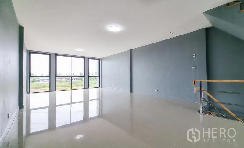 Shophouse for sale in Lam Luk Ka, Pathum Thani - Bright open-plan floor with glossy tiles and full-height windows facing greenery.