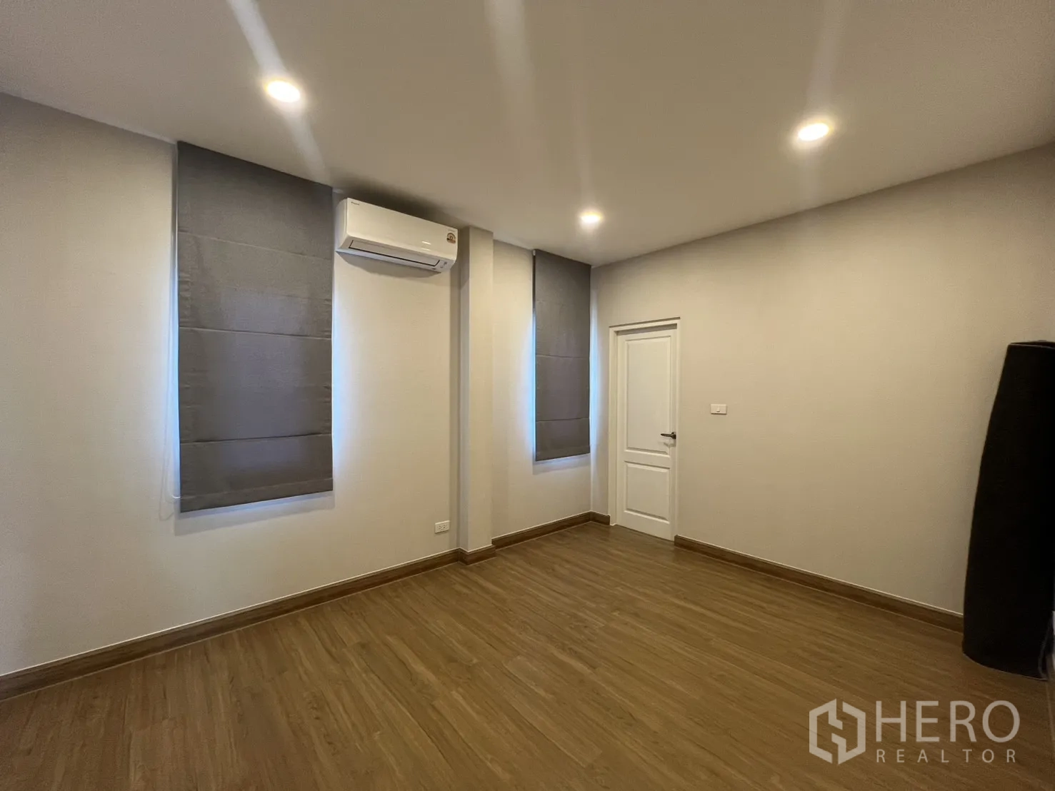 Detached House for rent in Lat Krabang, Bangkok - Bedroom view showing two window blinds, wood flooring, and a white door.