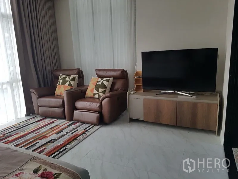 公寓 出租或出售在Bang Na, Bangkok - 卧室内舒适观影角，两张皮质躺椅、条纹地毯与电视柜。