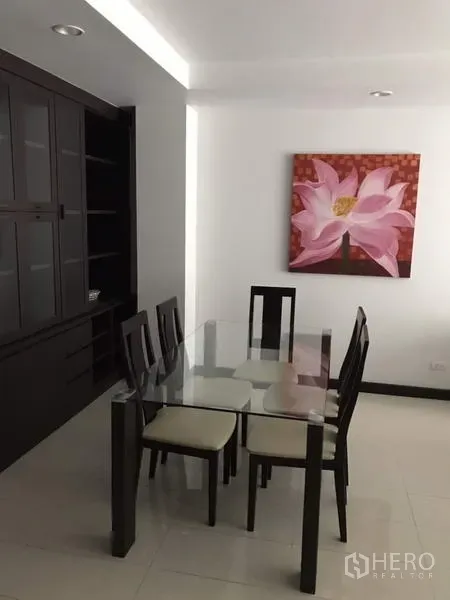 Condominium for rent in Watthana, Bangkok - Dining area with a glass-top table for six, dark built-in cabinetry and a lotus flower artwork on the wall.