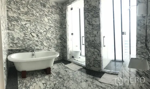 คอนโด ให้เช่าในBang Rak, Bangkok - ห้องน้ำหรูปูหินอ่อนโทนเทา‑ขาว พร้อมอ่างอาบน้ำเดี่ยวและห้องอาบน้ำกระจก